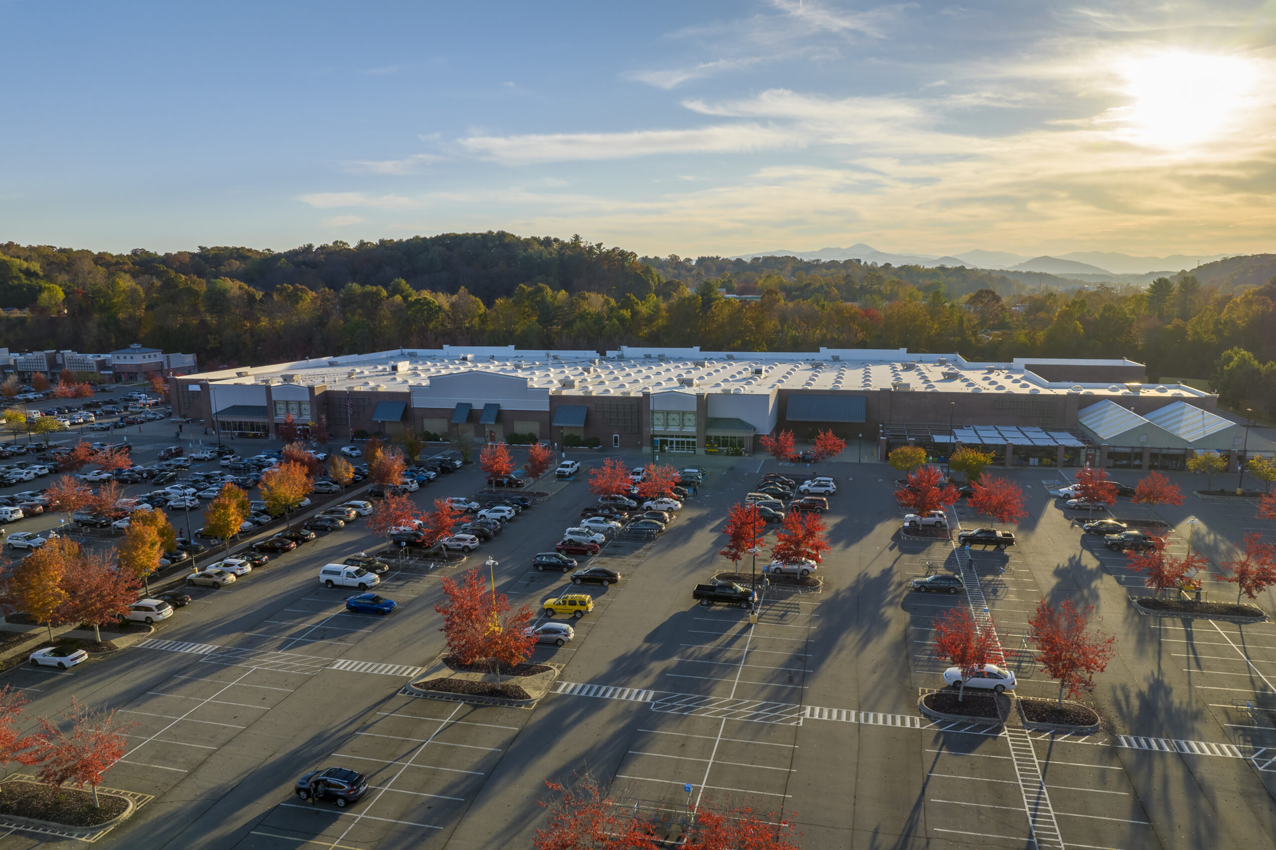 Aerial view of large parking lot in front of rgocery store with many parked colorful cars. Carpark at supercenter shopping mall with lines and markings for vehicle places and directions.