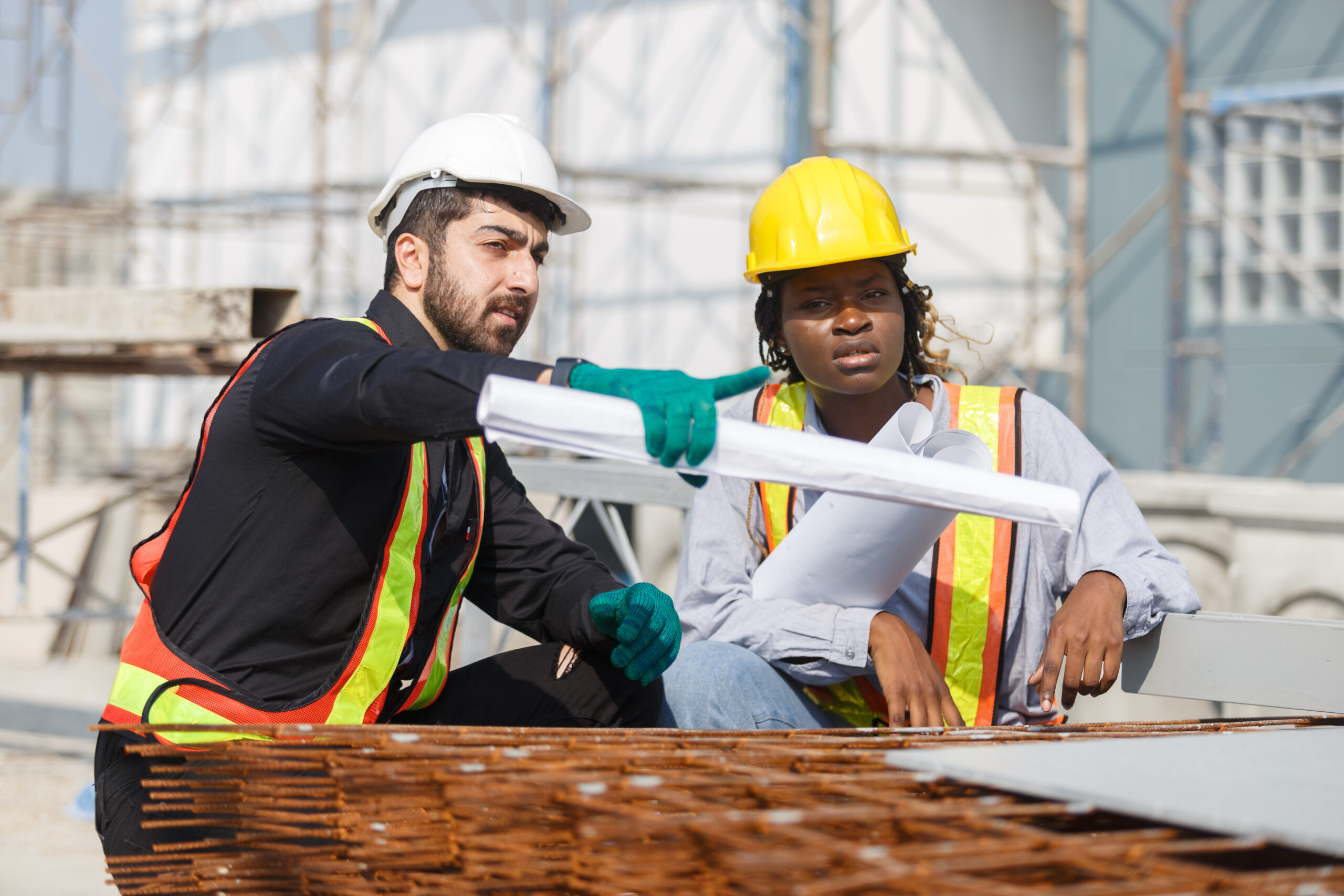 Construction civil engineer man and woman African American checking quality of work in construction site. Team of various nationalities working inspecting infrastructure building progress.